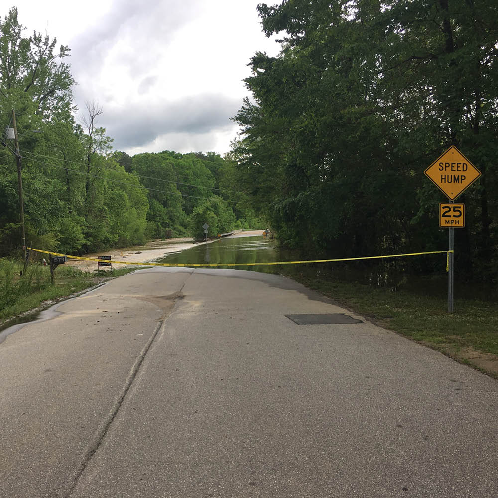 A road blocked off with yellow caution tape because water is flooding the area.